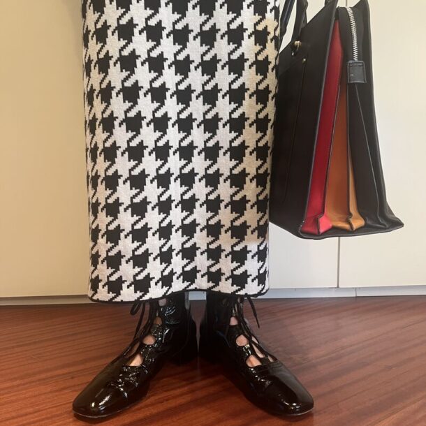 Zapatos negros estilo vintage con cordones, combinados con una falda de estampado pata de gallo y bolso de diseño con colores visibles.
