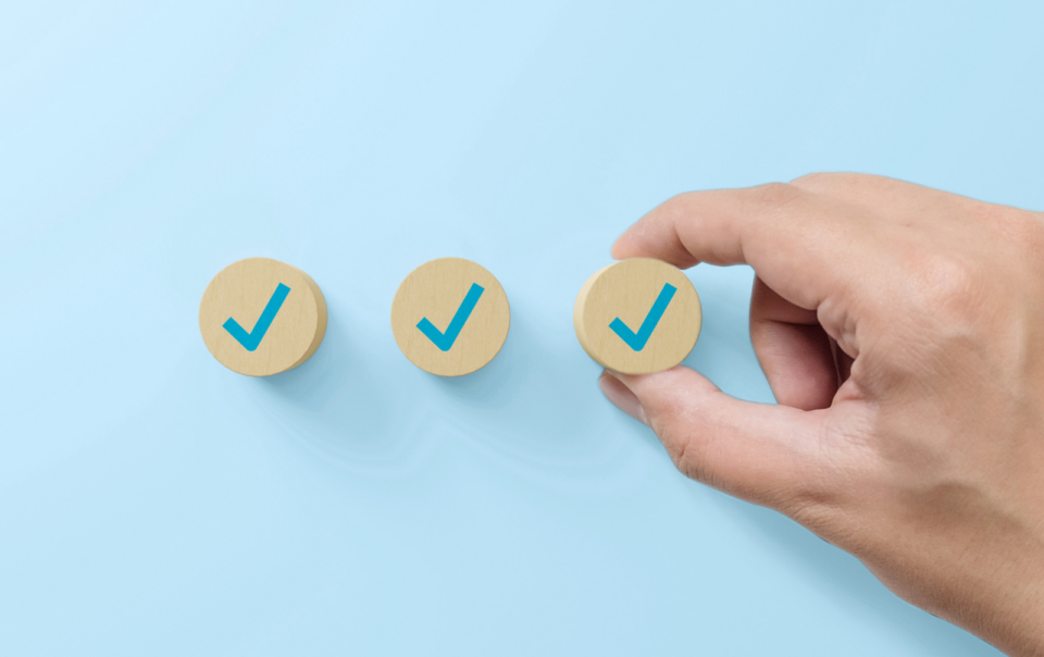 Mano colocando una ficha con un símbolo de verificación junto a otras dos sobre fondo azul, simbolizando seguimiento de objetivos y evaluación en liderazgo y gestión.