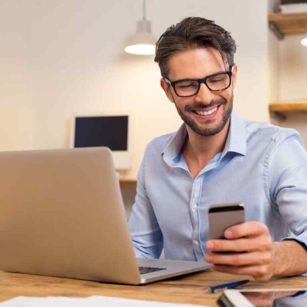 Hombre sonriente trabajando con su ordenador y teléfono, representando un liderazgo consciente y humano.