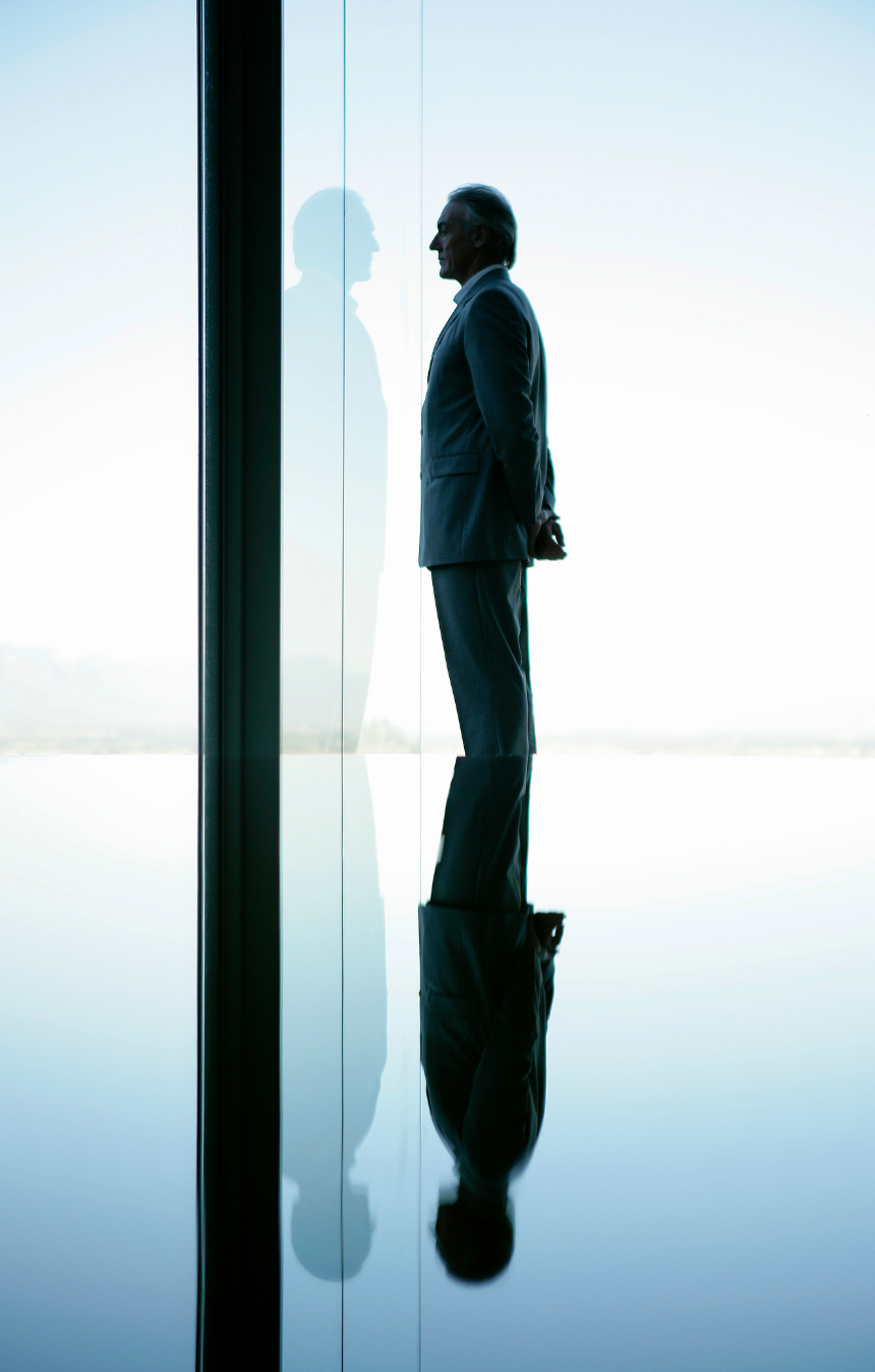 Hombre de negocios observando su reflejo en un cristal, simbolizando la introspección y el autoconocimiento en el liderazgo