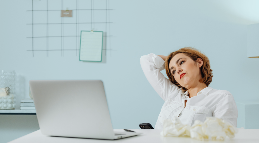 Profesional sentada frente al ordenador mostrando cansancio y tensión, simbolizando el desgaste emocional en el trabajo.