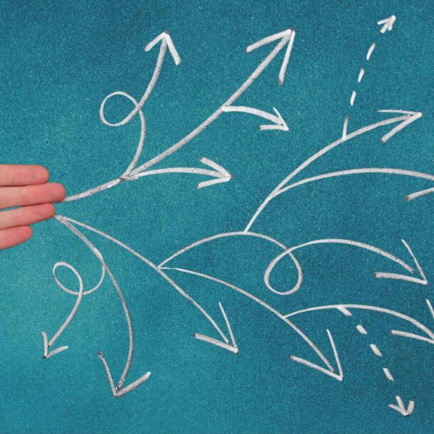 Mano extendida señalando múltiples flechas dibujadas que representan diferentes caminos y decisiones.