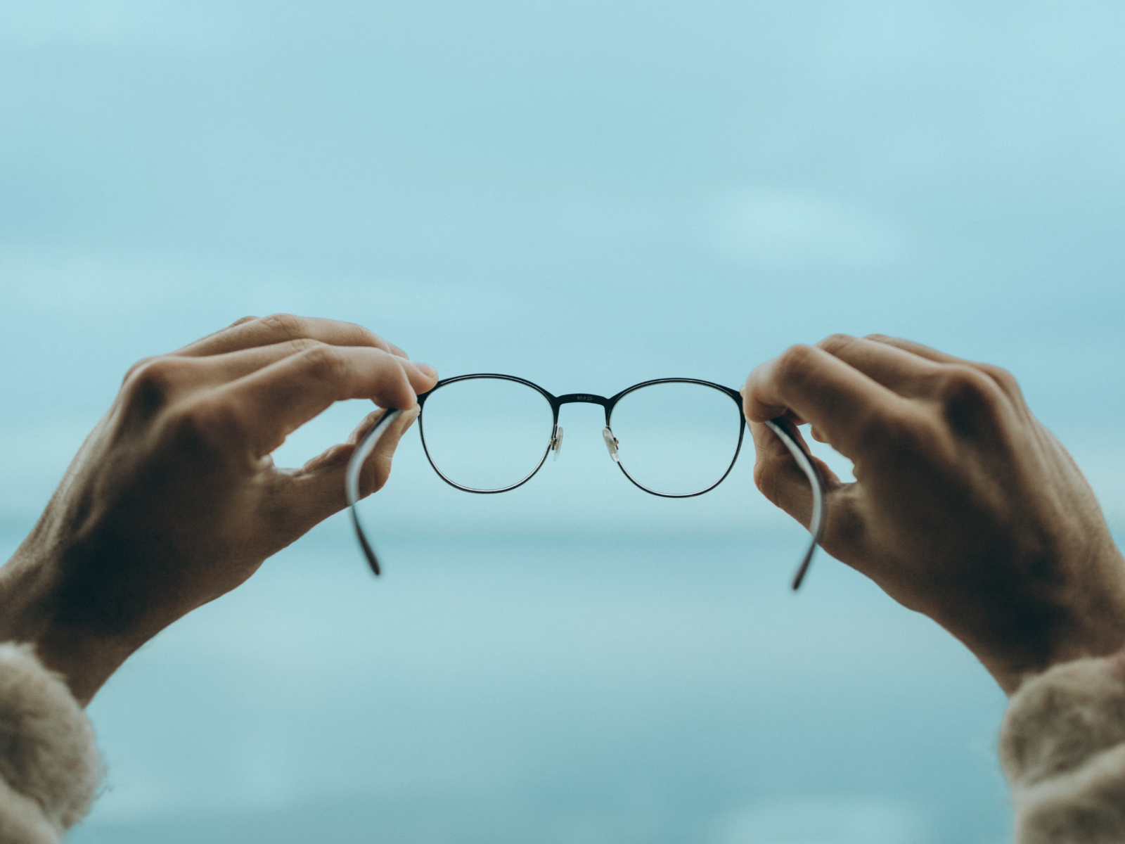 Dos manos sostienen unas gafas frente al cielo azul, una imagen que simboliza la claridad de visión y el autoconocimiento en el liderazgo.